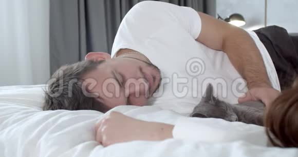 一个男人和他的女朋友和一只猫躺在床上抚摸着它4K视频的预览图