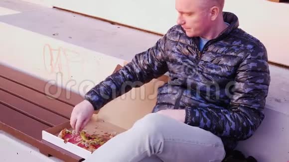 年轻的秃头坐在公园里从盒子里吃披萨他吃了辣椒挥了挥手视频的预览图