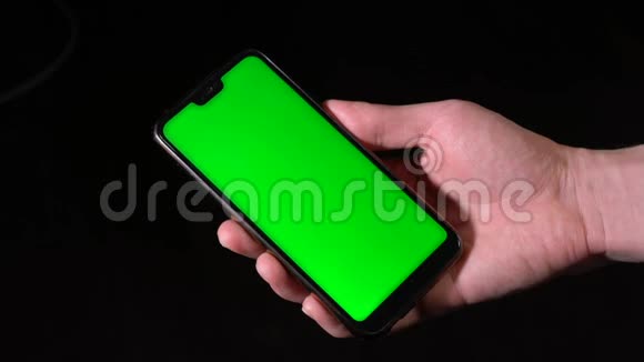 男性手拿着绿色屏幕的黑色手机视频的预览图