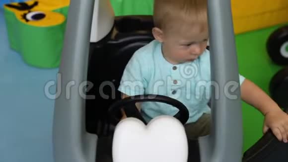婴儿在儿童的游戏中心驾驶玩具车一个男孩舵轮一岁的孩子视频的预览图