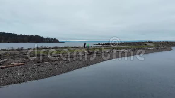 一个母亲和一个女儿在一个寒冷的冬天和他们的小狗在靠近海洋的狗公园散步的镜头视频的预览图