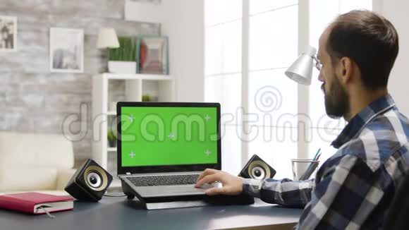 肩膀上放大镜头男人看着绿色屏幕的笔记本电脑视频的预览图