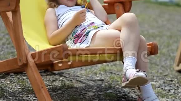 旅游女婴坐在甲板椅上带着太阳镜和帽子的小女孩在旅途中吃糖果和放松视频的预览图