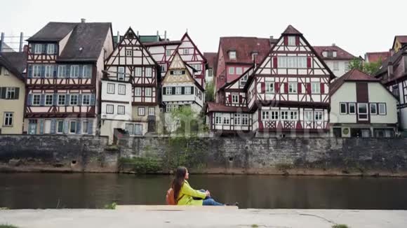穿着黄色外套的长头发女人背着背包坐在靠近水的地方背景是传统的半边视频的预览图