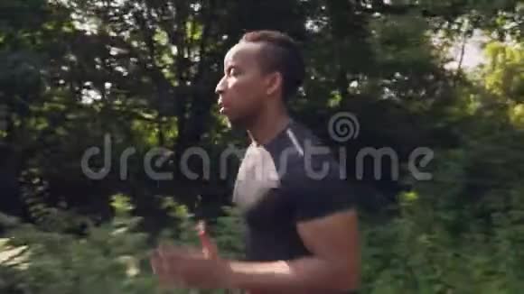 肌肉发达的非洲男子在绿色森林中奔跑的侧视视频的预览图