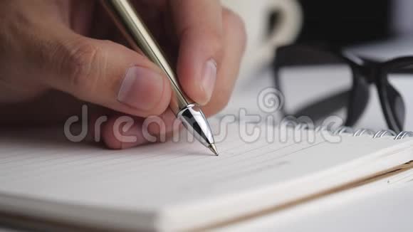 男性手写在螺旋记事本与各种物品放在白色桌面上视频的预览图