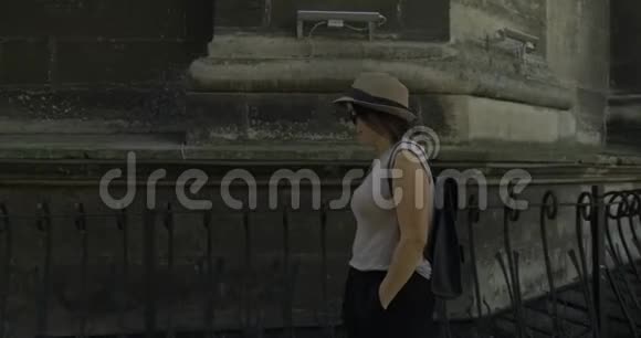 戴着帽子背着背包在中世纪城堡的石墙边散步的中年妇女微笑视频的预览图
