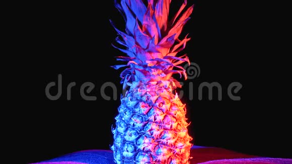 带有红色和蓝色背光的菠萝和水滴的微风在黑色背景下旋转视频的预览图