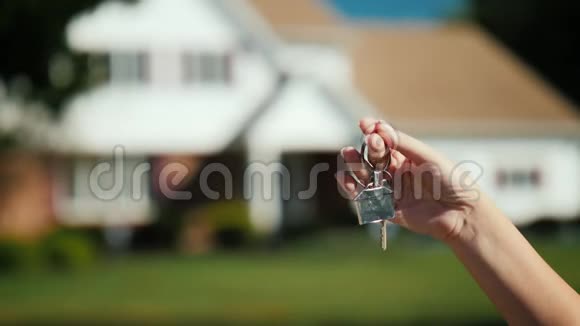 手拿着房子的钥匙在一个稍微模糊的典型美国房子的背景下视频的预览图