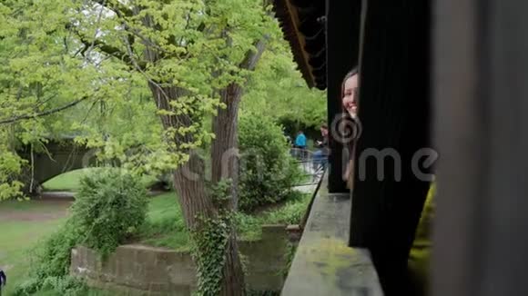 幸福的年轻女子从老木桥的柱子后面窥视视频的预览图
