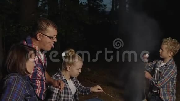 一家人在夏日森林的篝火上吃着热的棉花糖旅游家庭在森林里品尝烤棉花糖视频的预览图
