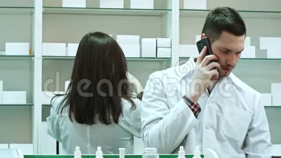 在药房工作的女性和男性药剂师通过智能电话交谈和检查药片视频的预览图