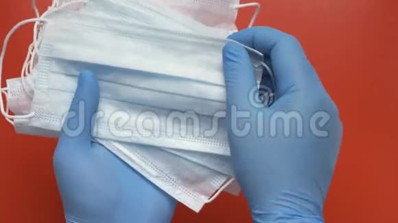 护理人员在红色背景下用蓝色医用手套保护手中的抗病毒口罩持有设备视频的预览图