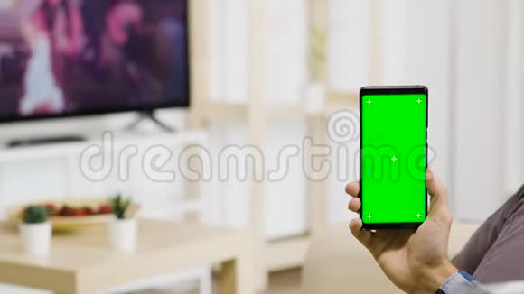在现代化光线充足的客厅里手里拿着一部绿色屏幕手机视频的预览图