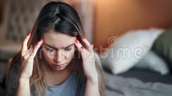 特写抑郁的女人按摩太阳穴感觉头痛坐在卧室的床上视频的预览图