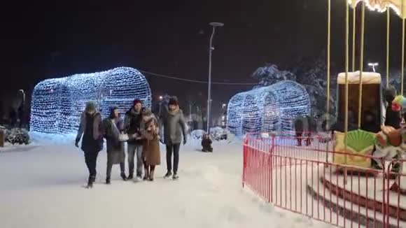 在大雪纷飞的冬夜朋友们在附近的旋转木马下散步玩得开心交流一群快乐的人视频的预览图