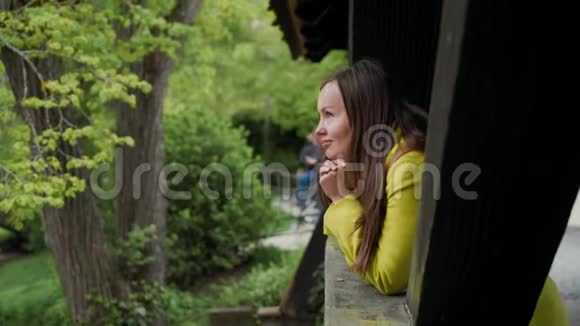 微笑的女孩从古老的木桥望着河的一侧绿色的景色侧面的景色视频的预览图