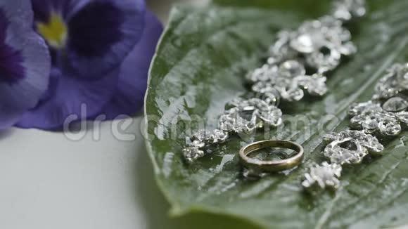 漂亮的耳环和一个金色的订婚戒指在一片潮湿的绿叶上视频的预览图