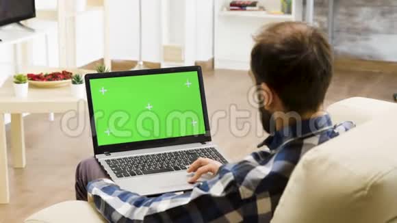 男人坐在沙发上腿上放着一台绿色屏幕笔记本电脑视频的预览图