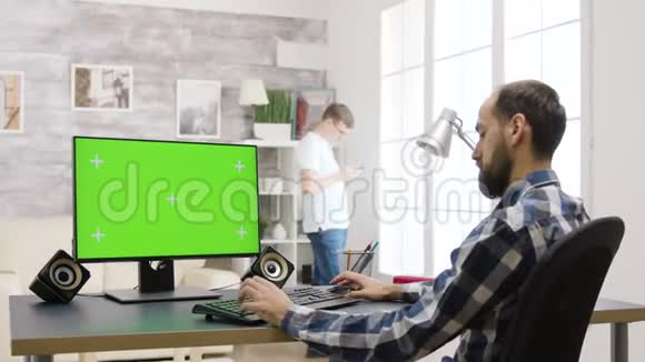 年轻人在明亮明亮的客厅里用绿色屏幕工作视频的预览图