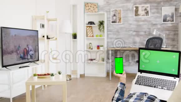 在明亮明亮的客厅里男人手里拿着和手机上面有绿色的屏幕视频的预览图
