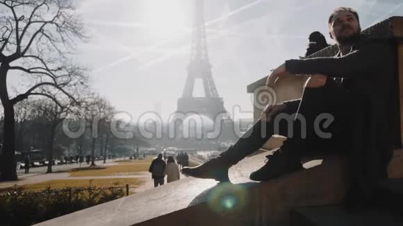 体贴英俊浪漫的欧洲游客坐在史诗般的巴黎埃菲尔铁塔日落天空全景慢动作视频的预览图