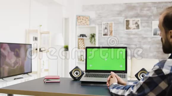 静态镜头男人看绿色屏幕笔记本电脑视频的预览图