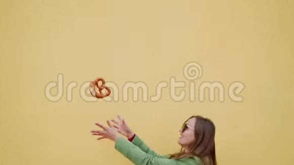 微笑的快乐女孩在黄色的背景下向空中投掷传统的巴伐利亚椒盐卷饼视频的预览图