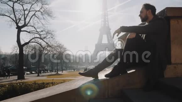英俊浪漫的高加索旅行博主男子坐在令人惊叹的巴黎埃菲尔铁塔日出天景慢动作视频的预览图