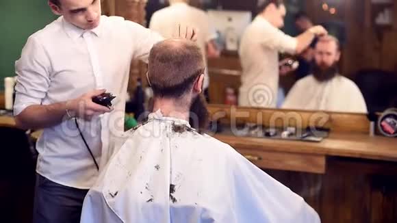 年轻的理发师用电动剃须刀做自信的动作男人理发坐在镜子前的镜头前视频的预览图