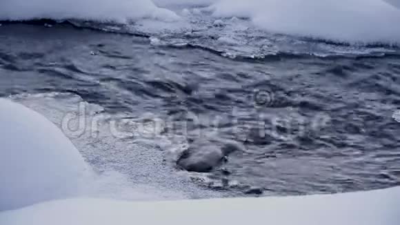黑暗的冷水在冰雪中流动雪林中的溪流视频的预览图