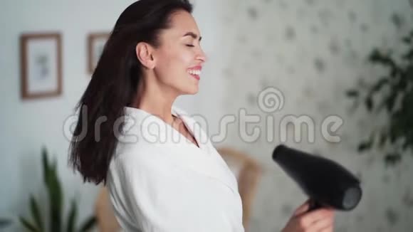侧视妇女穿着白色浴袍用吹风机擦干头发动作缓慢视频的预览图