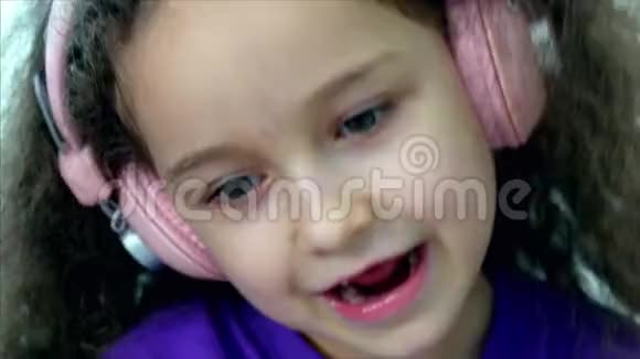 一个留着卷发的可爱孩子的肖像穿着一件带粉色耳机的紫色T恤的白种人小女孩视频的预览图