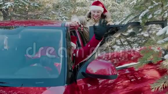 戴着红色圣诞帽的快乐男人就像圣诞老人在白雪皑皑的森林里从车里挥手新年快乐的一对视频的预览图