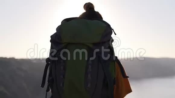 一个背着旅游背包的女孩走在悬崖边停在边上伸出双手欣赏视频的预览图