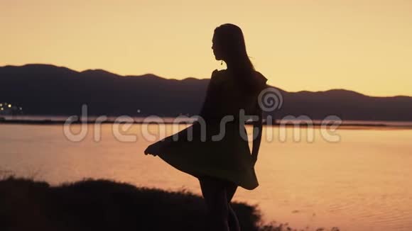 女人的剪影看着海滩上金色的日落风吹着衣服慢动作视频的预览图