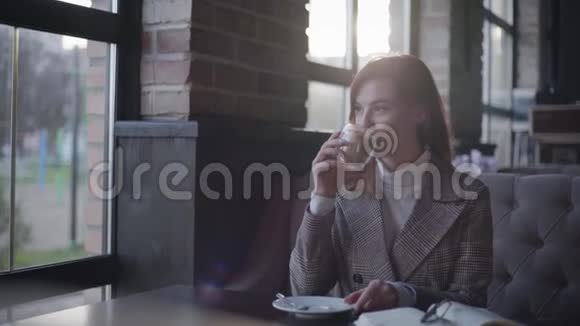 咖啡馆里的女孩年轻漂亮的女人在午餐时间享受放松一边喝咖啡一边看窗外视频的预览图