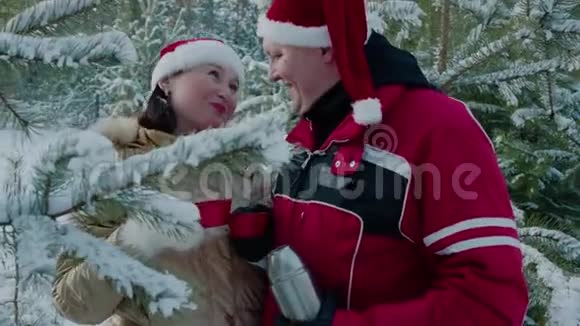 一对戴着红色圣诞帽的浪漫情侣在雪林里喝着热水瓶里的热茶爱喝酒的男女视频的预览图