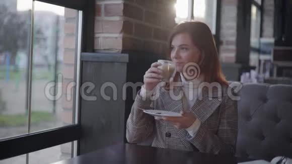有魅力的美丽女性在午休时喝咖啡坐在窗外欣赏风景的肖像视频的预览图