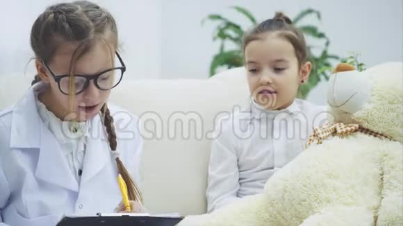 两个可爱的孩子在玩泰迪熊一个女孩是医生脖子上戴着听诊器另一个是泰迪的主人视频的预览图