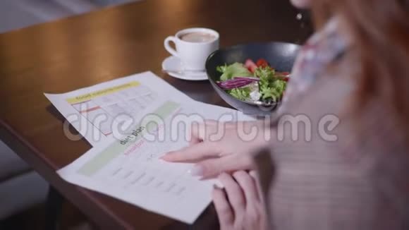 饮食计划及时的年轻漂亮女孩监测她的饮食并计算卡路里含量坐在餐桌上的咖啡馆概念视频的预览图