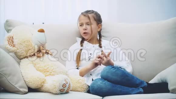 可爱的小女孩坐在沙发上和她的泰迪说话拼命地解释知道它不明白视频的预览图