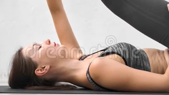 近距离呼吸年轻的瑜伽女子抬起腿躺在地上伸展身体视频的预览图