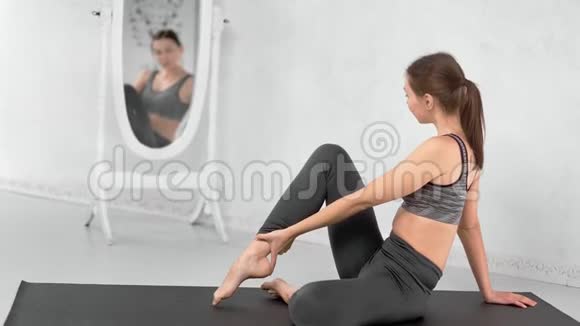 健身年轻女性灵活的身体练习伸展在垫子上看镜子视频的预览图