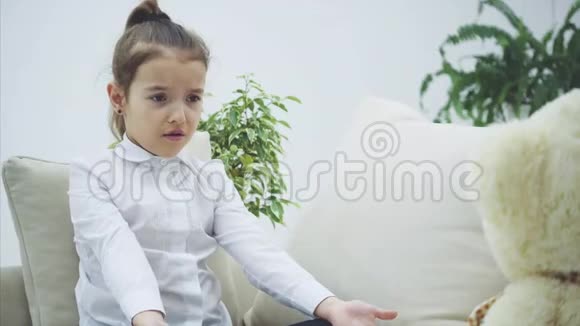 可爱的小女孩坐在沙发上和她的泰迪说话它不了解她她看起来很失望视频的预览图