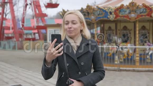 一个女人走在一个废弃的游乐园里在视频聊天有影响力的人制造智能手机视频的预览图