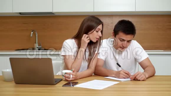 年轻夫妇正在厨房里聊天并在记事本条目上写字视频的预览图