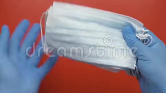 医生在红色背景下用蓝色医用手套保护手中的抗病毒口罩视频的预览图