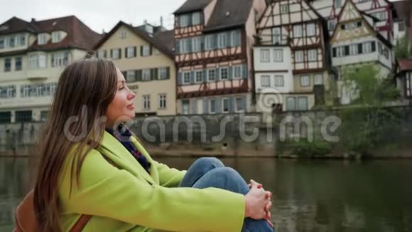 穿着黄色外套和背包的漂亮女人的肖像年轻女子坐在水边看着传统的德国视频的预览图