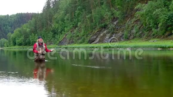 在山上的河边钓鱼一个穿着红色衣服头上戴着绷带的老人扔苍蝇渔具运动或h视频的预览图